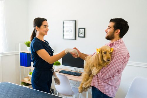 female-vet-greeting-male-pet-owner-who-is-holding-his-dog